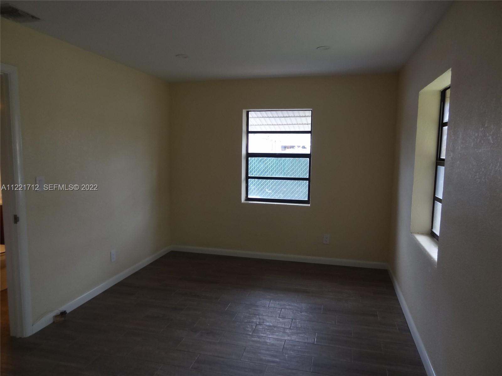 An empty bedroom features light-colored walls, dark wood-look tile flooring, and two windows — 2212 Johnson St, Hollywood FL 33020, HOLLYWOOD, FL