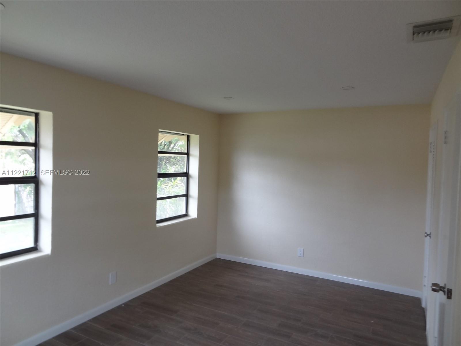 An empty room features light-colored walls, dark wood-look flooring, two windows, and a white door — 2212 Johnson St, Hollywood FL 33020, HOLLYWOOD, FL