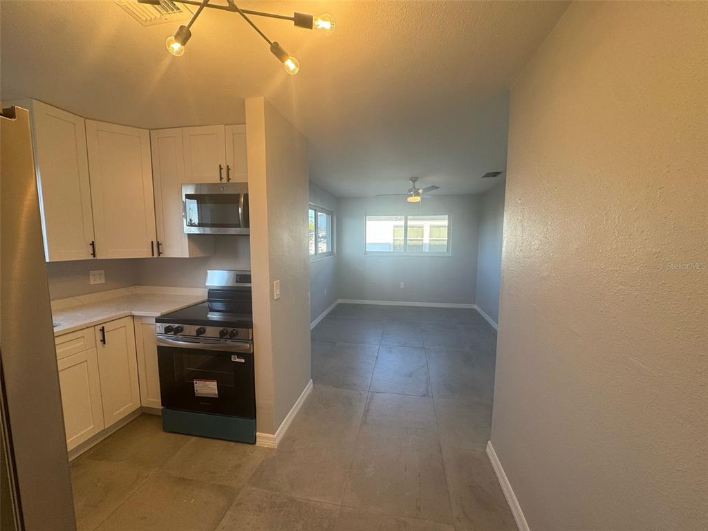 A kitchen with white cabinets and stainless steel appliances opens into a tiled living area — 342 51ST AVENUE N, ST PETERSBURG, FL