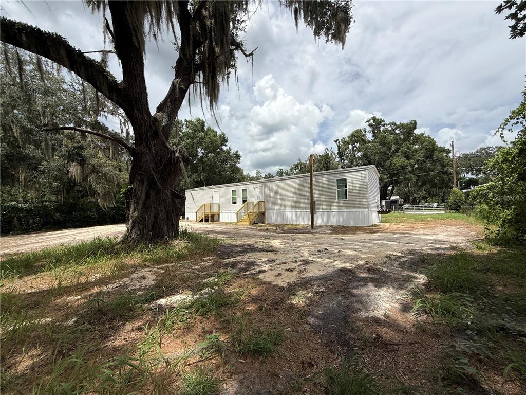 A single-story manufactured home sits on a dirt lot beneath a large, moss-covered oak tree — 5642 MEADOW GLEN ROAD, LAKELAND, FL