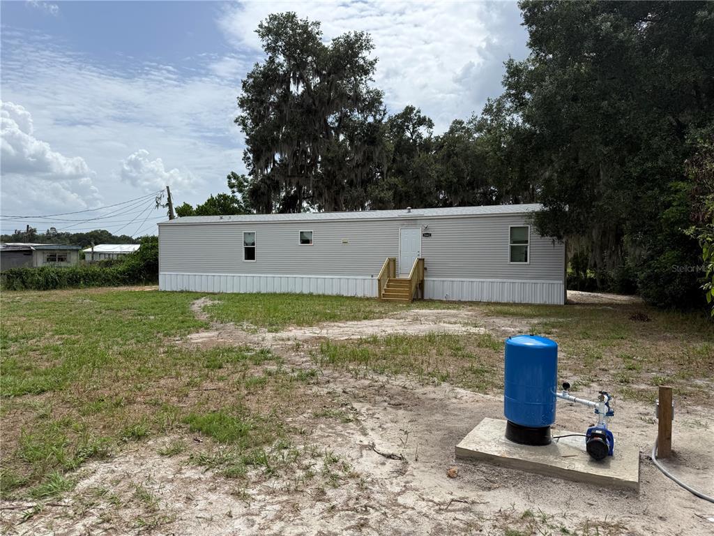 A light-colored manufactured home sits on a grassy lot with a blue well tank — 5642 MEADOW GLEN ROAD, LAKELAND, FL