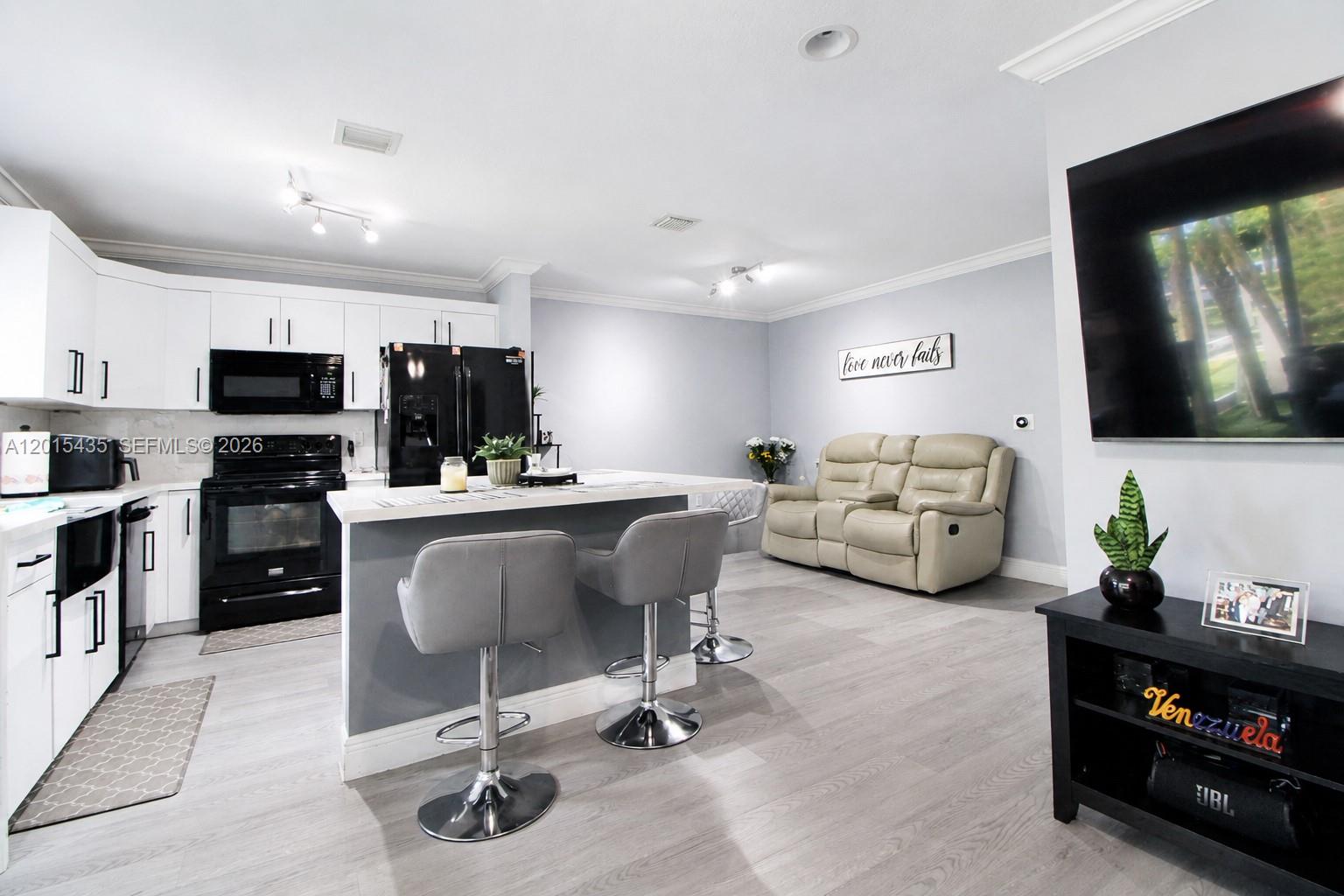 A modern kitchen with white cabinets and black appliances opens into a living area — 4946 SW 66th Ter, Davie FL 33314, DAVIE, FL