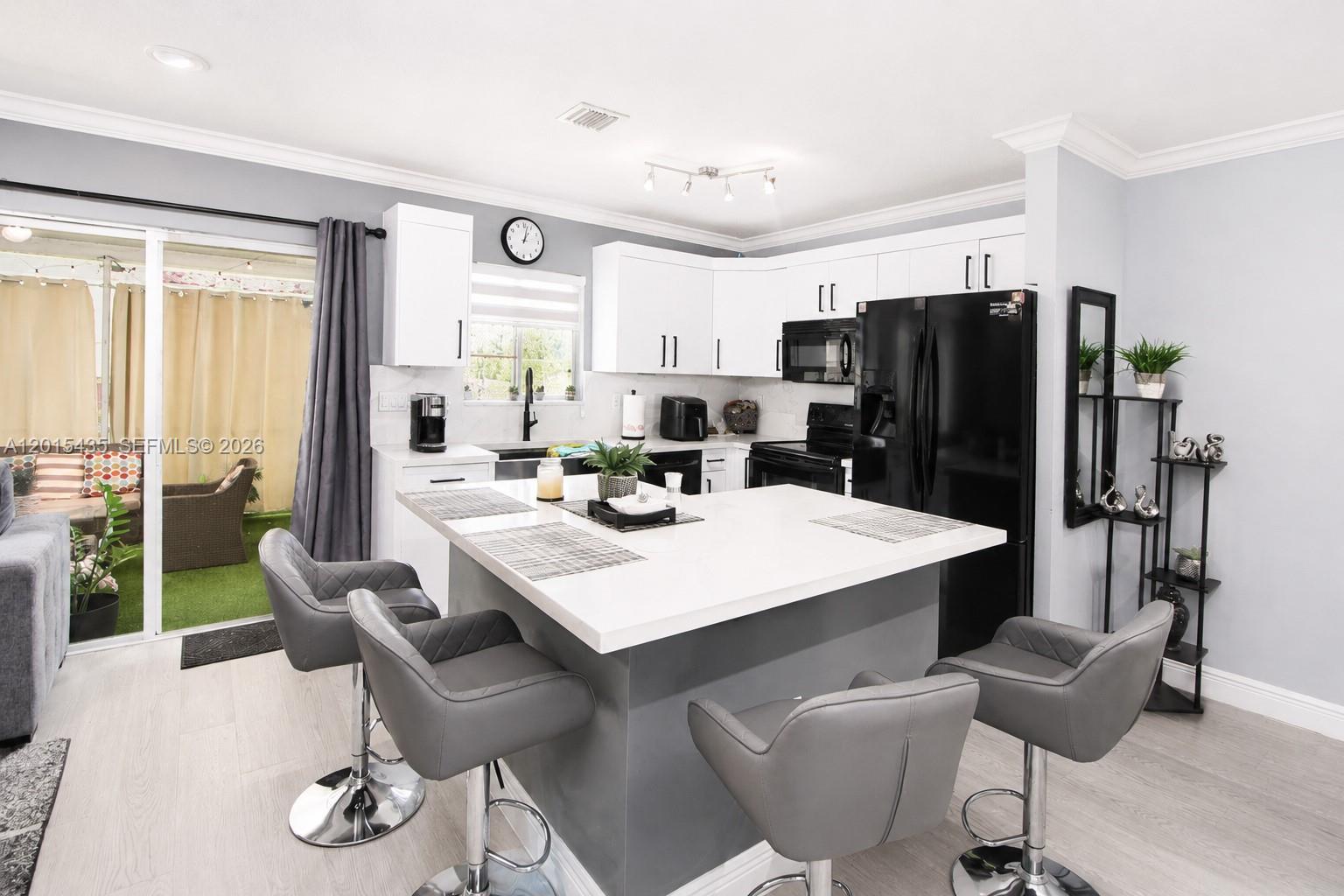 A modern kitchen features a central island with bar seating, white cabinets, and black appliances — 4946 SW 66th Ter, Davie FL 33314, DAVIE, FL