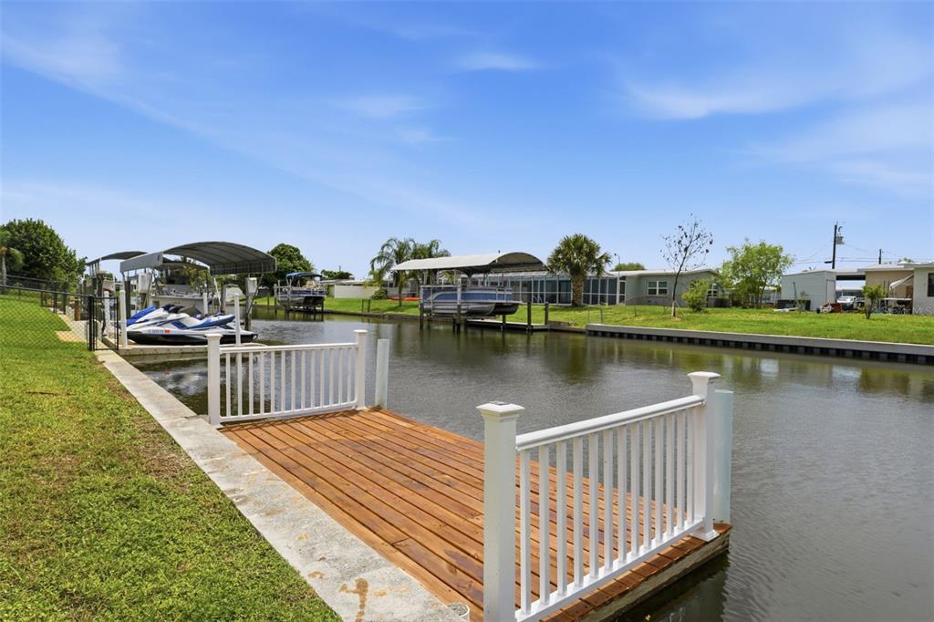 A wooden dock with white railings sits on a canal next to boat lifts — 178 DOWLING AVENUE NE, PORT CHARLOTTE, FL