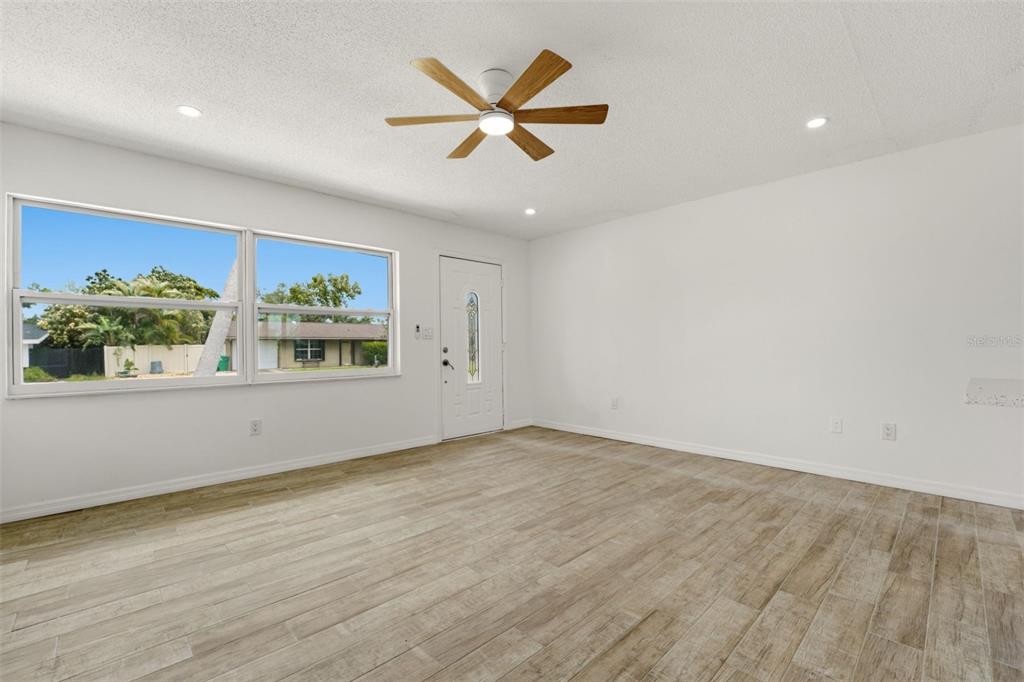 A bright living room features light wood-look tile flooring, white walls, and a ceiling fan — 178 DOWLING AVENUE NE, PORT CHARLOTTE, FL
