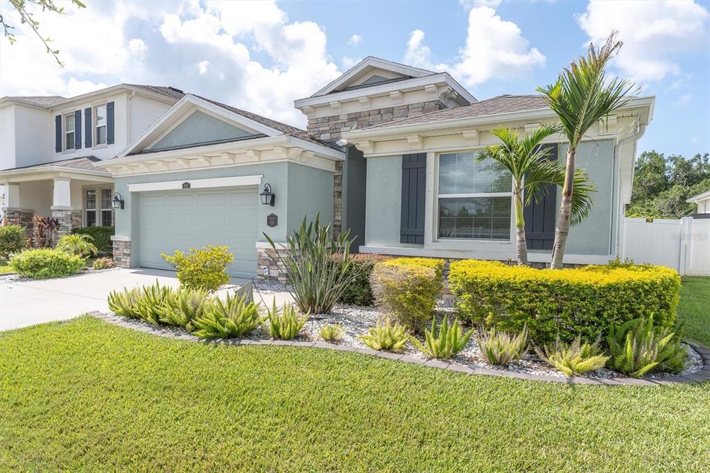 The exterior of a single-story house with a light green facade, stone accents, and landscaping — 8110 PRAISE DRIVE, TAMPA, FL