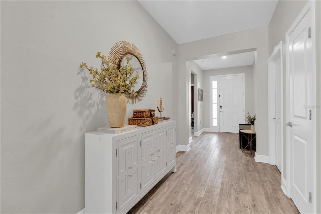A bright hallway features light wood-look flooring, a white console table, and a sunburst mirror — 8110 PRAISE DRIVE, TAMPA, FL