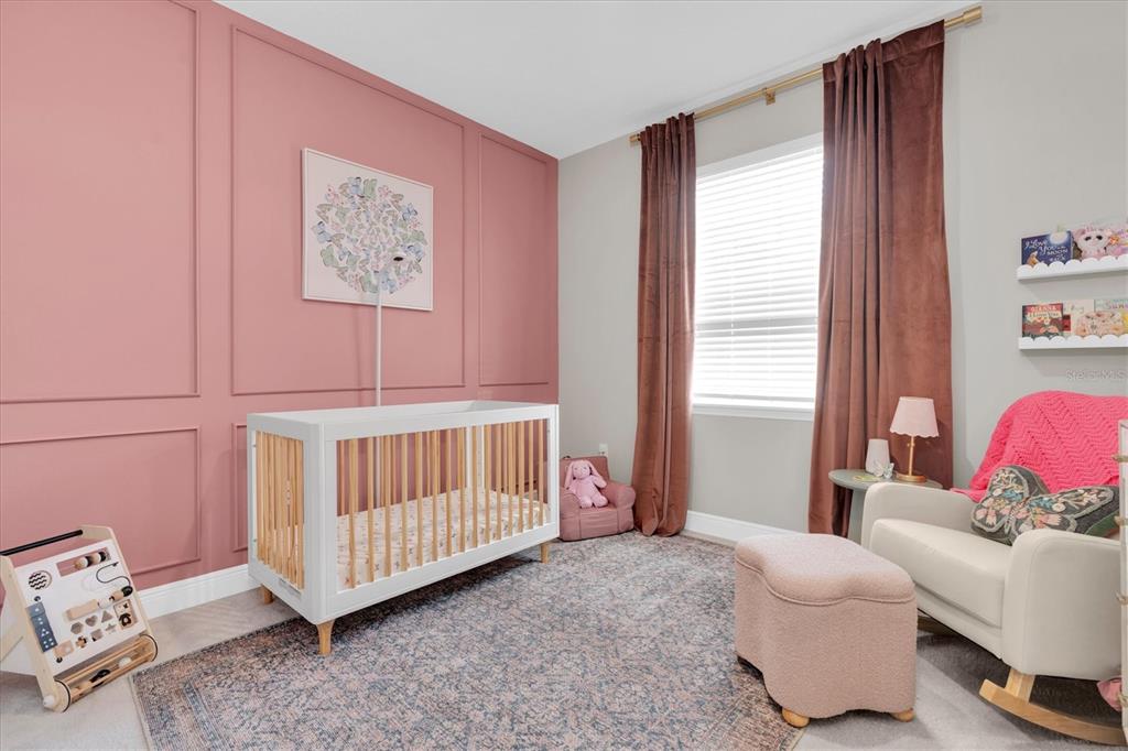 A nursery features a white crib, a pink accent wall with molding, and a rocking chair — 8110 PRAISE DRIVE, TAMPA, FL