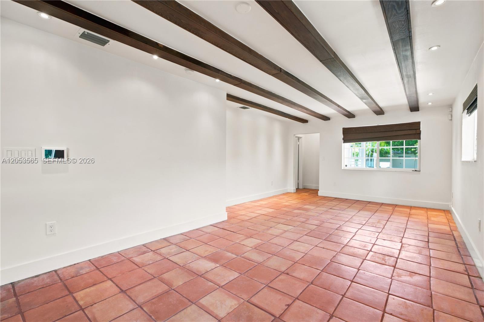 An empty room features terracotta tile flooring, white walls, and dark wood ceiling beams — 3945 SW 61st Ave, Miami FL 33155, MIAMI, FL