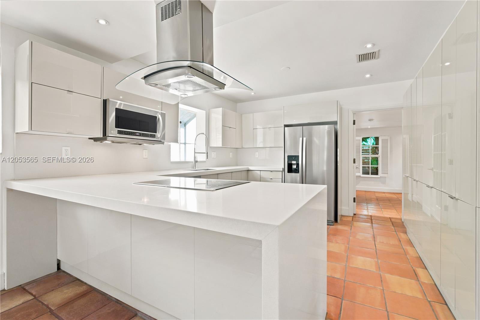 A modern white kitchen features a large island, stainless steel appliances, and terracotta tile flooring — 3945 SW 61st Ave, Miami FL 33155, MIAMI, FL