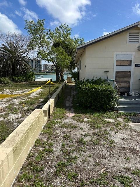 A concrete block house exterior features a side entrance and a low retaining wall — 12620 LAGOON LANE, TREASURE ISLAND, FL