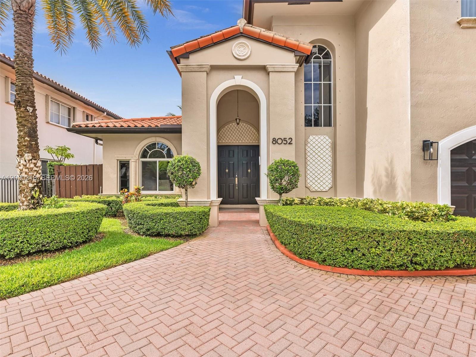 The exterior of a house features a brick walkway leading to a dark double door — 8052 NW 161st Ter, Miami Lakes FL 33016, MIAMI LAKES, FL