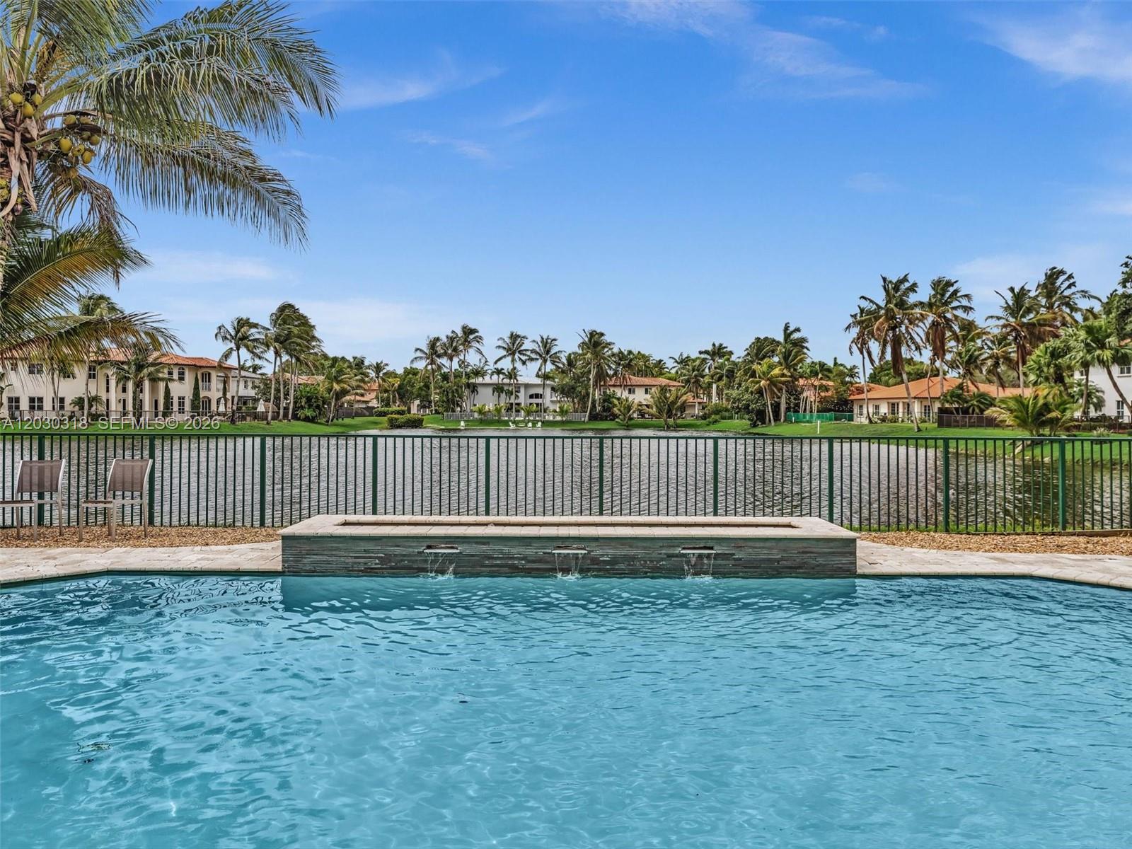 A swimming pool with a water feature overlooks a lake and palm trees — 8052 NW 161st Ter, Miami Lakes FL 33016, MIAMI LAKES, FL