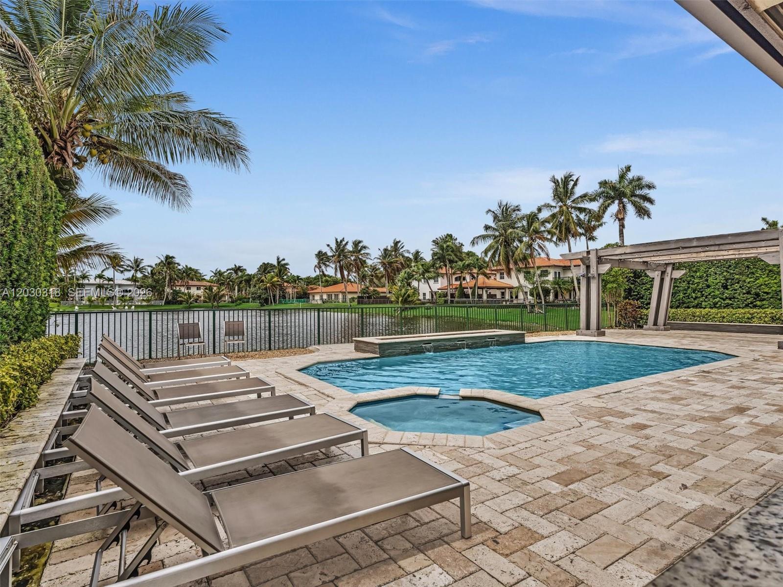 A swimming pool and spa sit on a stone patio overlooking a lake and palm trees — 8052 NW 161st Ter, Miami Lakes FL 33016, MIAMI LAKES, FL