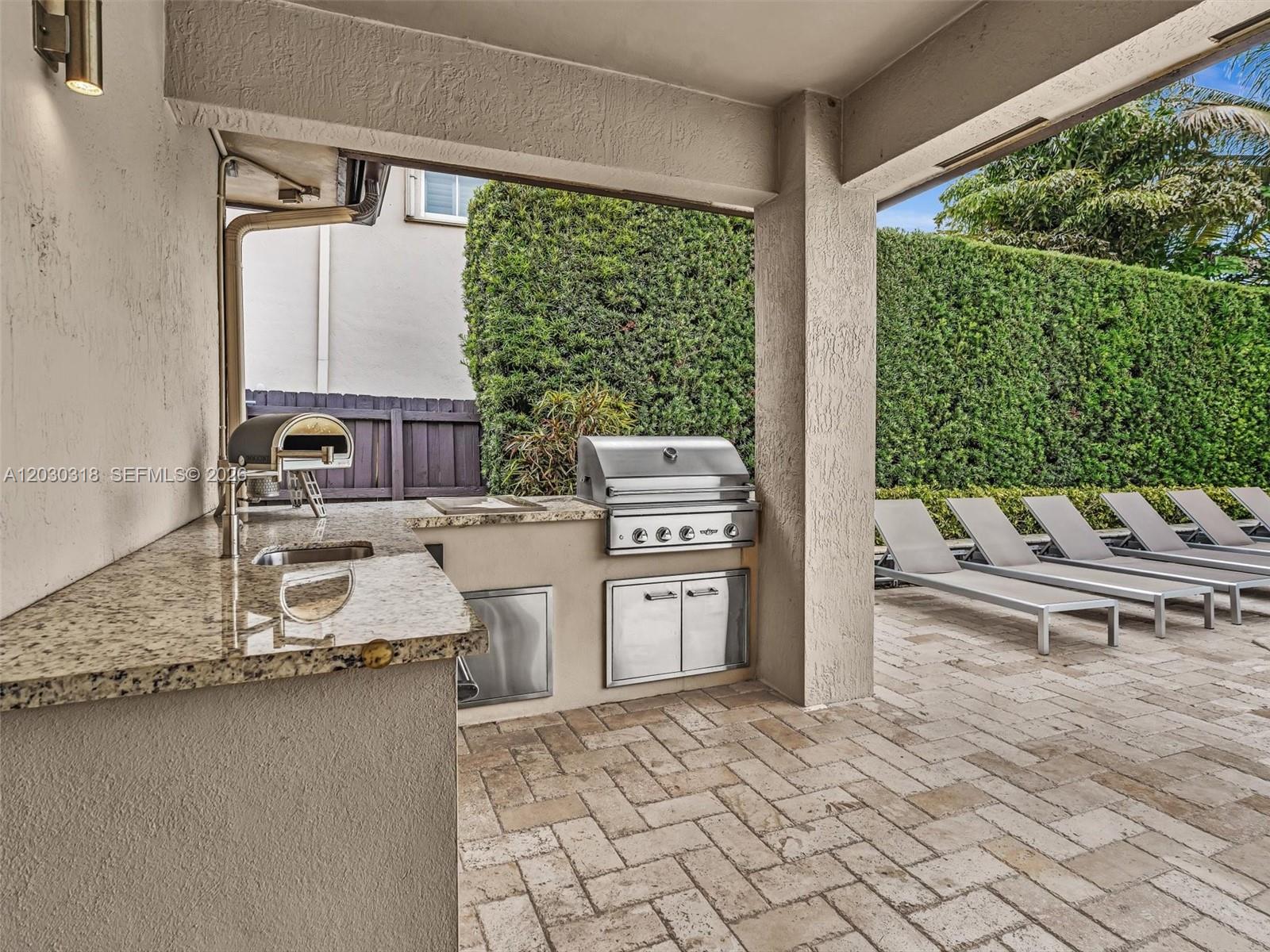 An outdoor kitchen features a stainless steel grill, pizza oven, and granite countertops on a patio — 8052 NW 161st Ter, Miami Lakes FL 33016, MIAMI LAKES, FL