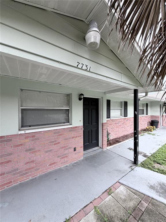 A covered entryway features a black door, brick siding, and a light fixture above — 7731 CHAPEL AVENUE, PORT RICHEY, FL
