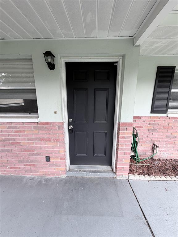 A black front door is centered on a brick and light-colored exterior wall — 7731 CHAPEL AVENUE, PORT RICHEY, FL