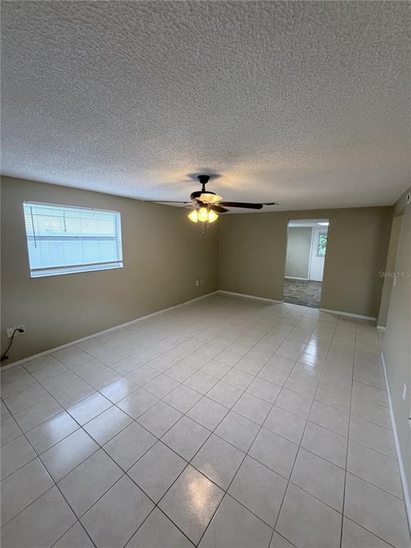 An empty room with beige walls, a white tiled floor, and a ceiling fan — 7731 CHAPEL AVENUE, PORT RICHEY, FL