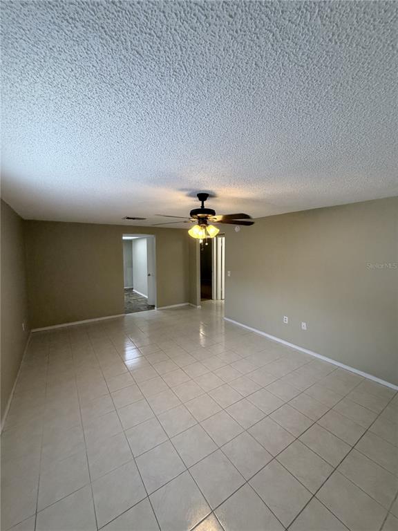 A living room with beige walls, a popcorn ceiling, a ceiling fan, and tiled flooring — 7731 CHAPEL AVENUE, PORT RICHEY, FL