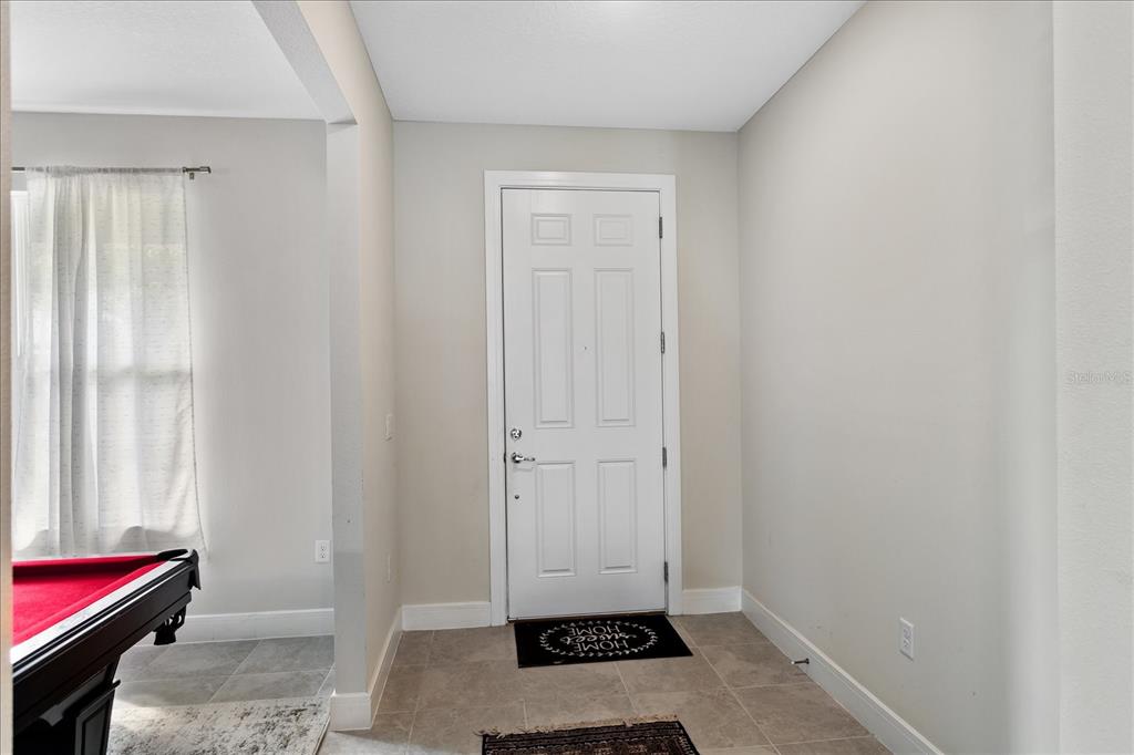 An entryway features a white front door, tiled flooring, and a partial view of a pool table — 3980 MEANDERING BAY DRIVE, APOPKA, FL