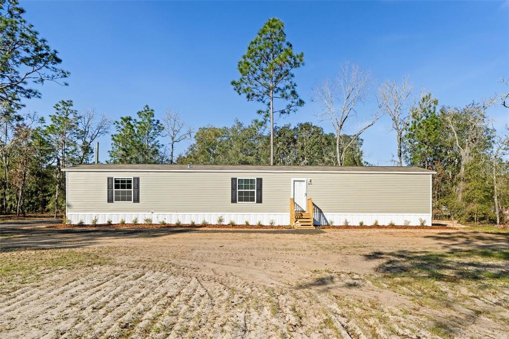 A single-story manufactured home with light siding sits on a dirt lot among trees — 5370 NE 108TH TERRACE, BRONSON, FL