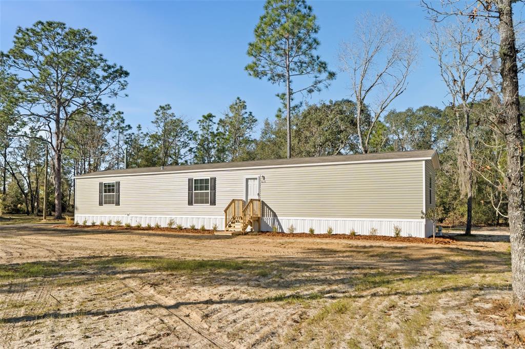 A single-story manufactured home with light green siding sits on a sandy lot among trees — 5370 NE 108TH TERRACE, BRONSON, FL