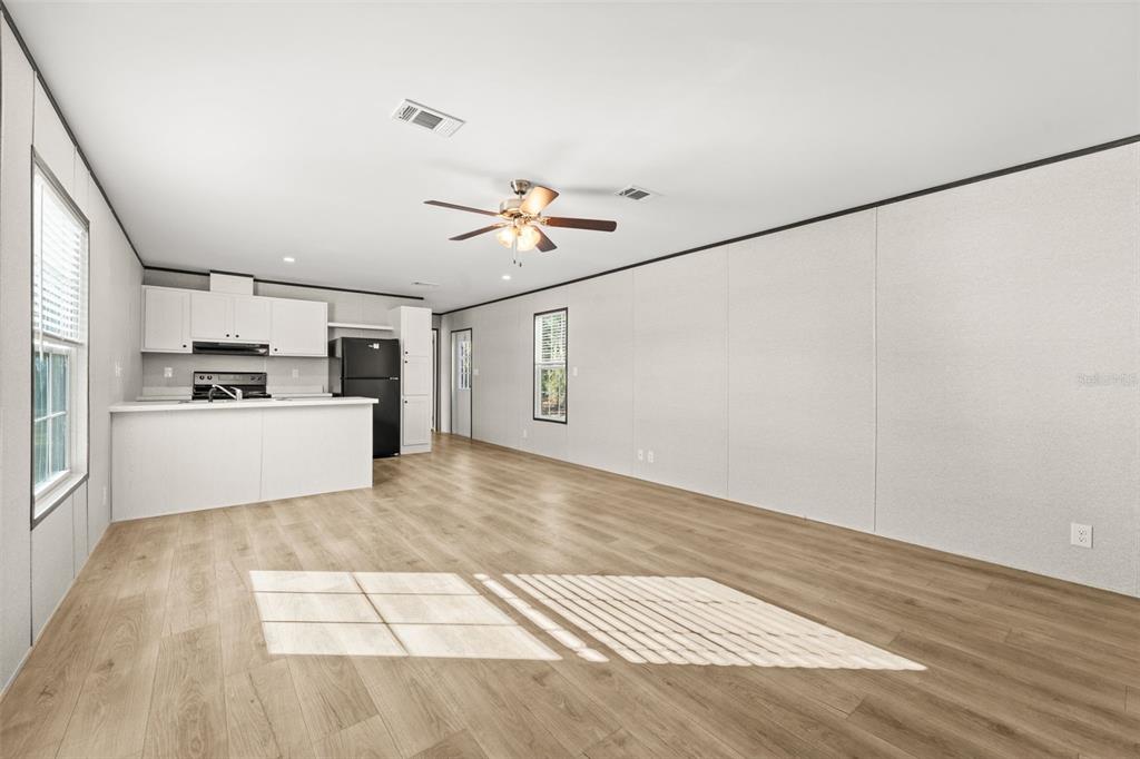 An open-concept living area with light wood flooring, white walls, and an adjacent kitchen — 5370 NE 108TH TERRACE, BRONSON, FL