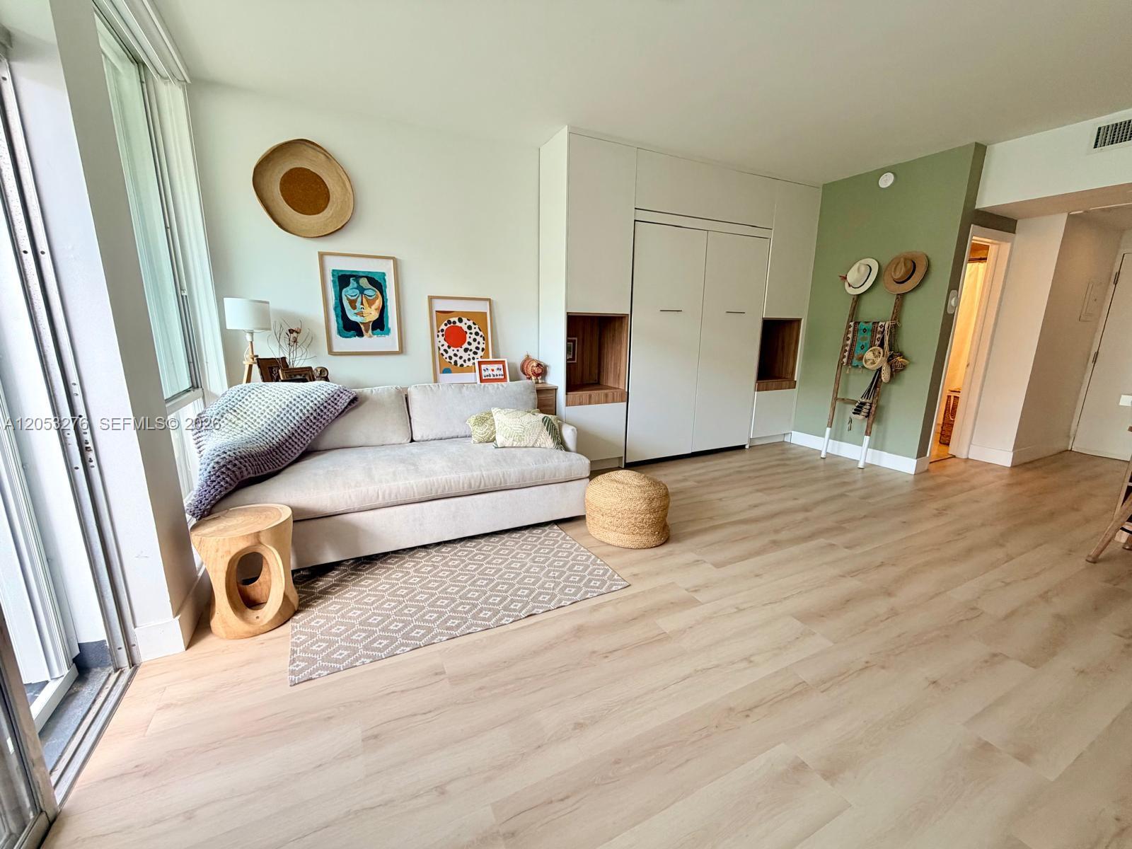 A living room features light wood flooring, a sofa, a wall bed, and green accents — 700 Biltmore Way # 308, Coral Gables FL 33134, CORAL GABLES, FL