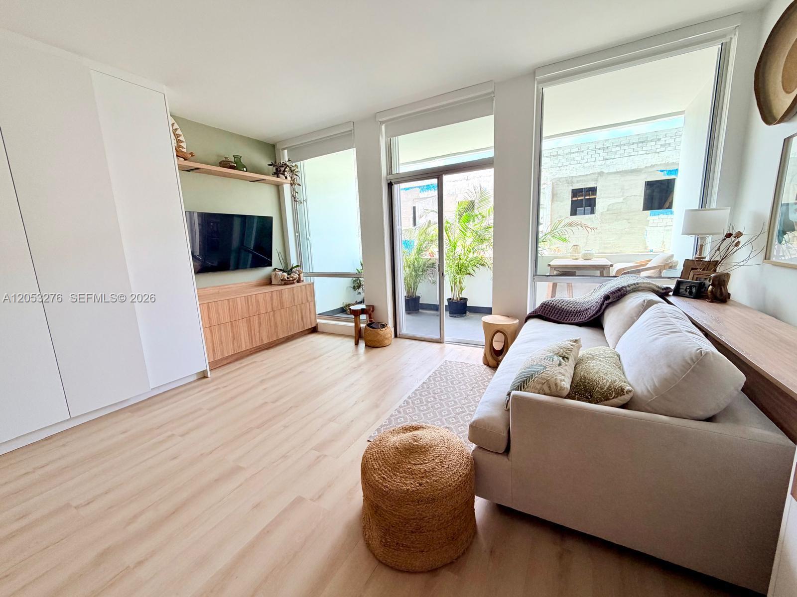 A modern living room features light wood flooring, a beige sofa, and a balcony view — 700 Biltmore Way # 308, Coral Gables FL 33134, CORAL GABLES, FL