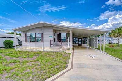 A single-story manufactured home features a light-colored exterior, a covered carport, and a grassy yard — 35151 COLONY HILLS DRIVE, ZEPHYRHILLS, FL