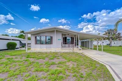 A single-story manufactured home features light siding, a brick base, and an attached carport — 35151 COLONY HILLS DRIVE, ZEPHYRHILLS, FL