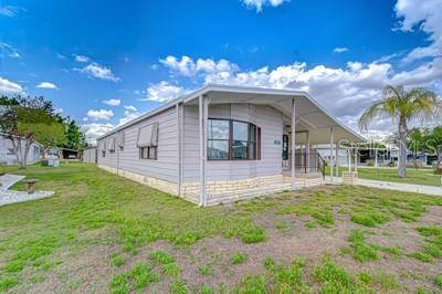 A light gray manufactured home with a covered carport sits on a grassy lot — 35151 COLONY HILLS DRIVE, ZEPHYRHILLS, FL