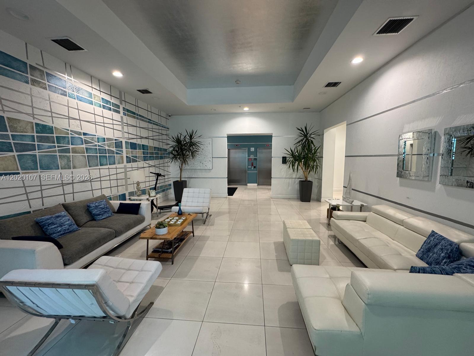 A modern lobby features white tile floors, two seating areas, and a decorative blue-tiled wall — 1723 SW 2nd Ave # 704, Miami FL 33129, MIAMI, FL