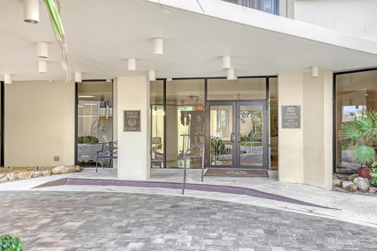 The exterior entrance of a building features a paved driveway, glass doors, and signage — 2800 N Ocean Drive # 3c, Riviera Beach FL 33404, RIVIERA BEACH, FL