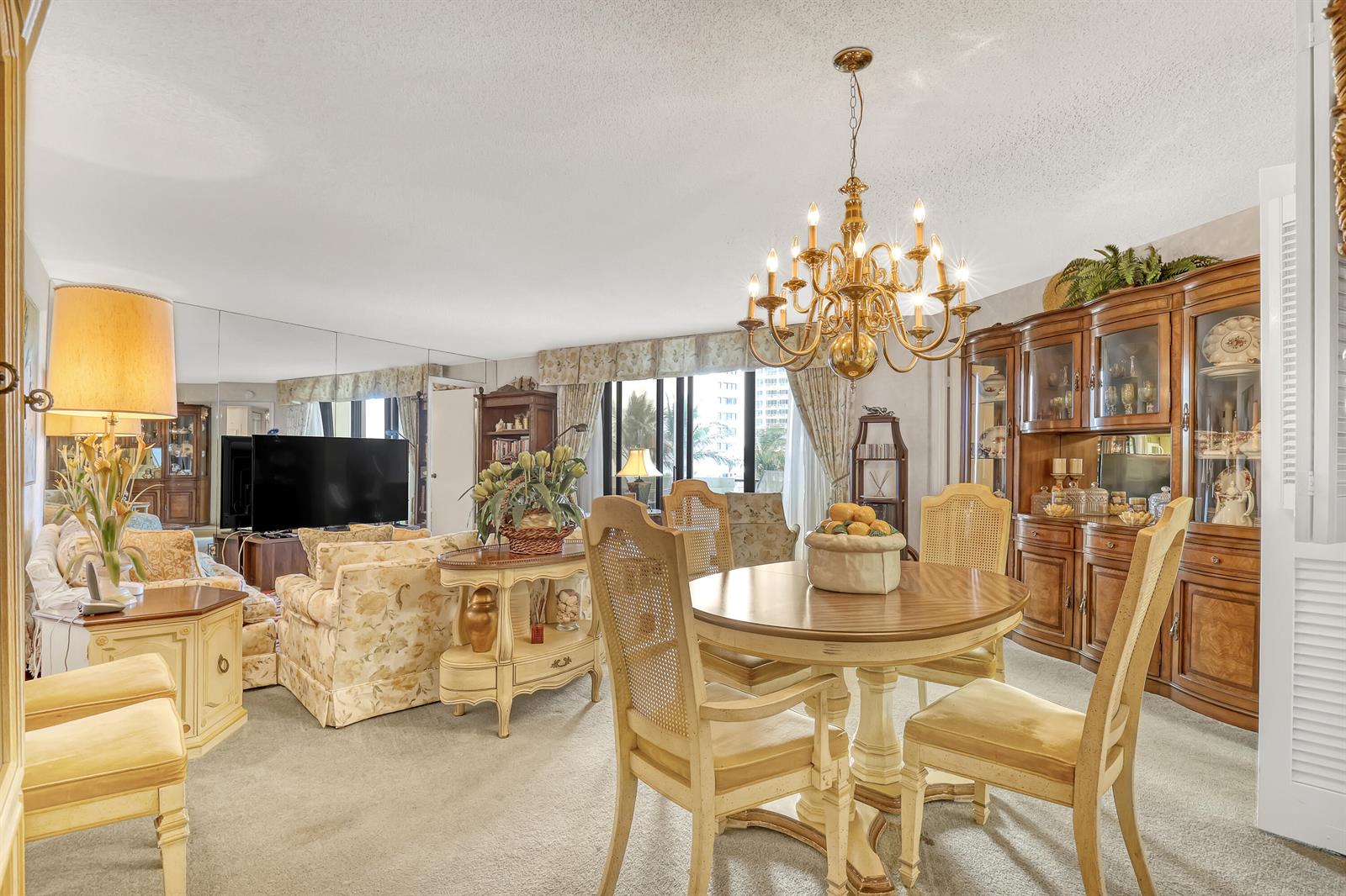 A dining area and living room with a chandelier, wooden hutch, and floral furniture — 2800 N Ocean Drive # 3c, Riviera Beach FL 33404, RIVIERA BEACH, FL