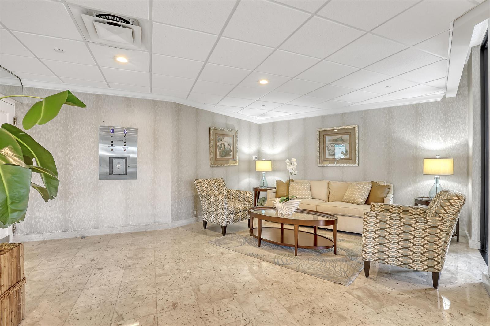 A lobby seating area features a beige sofa, two patterned armchairs, and a glass coffee table — 2800 N Ocean Drive # 3c, Riviera Beach FL 33404, RIVIERA BEACH, FL