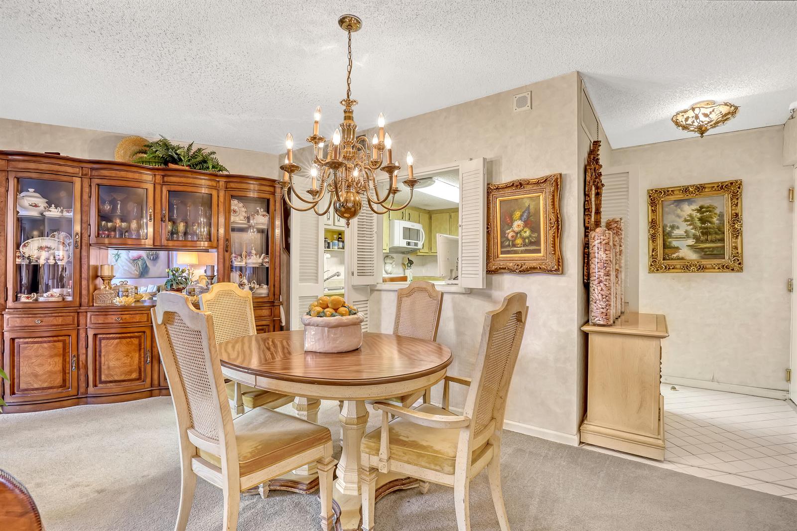A dining room features a round wooden table, cane-back chairs, a chandelier, and a hutch — 2800 N Ocean Drive # 3c, Riviera Beach FL 33404, RIVIERA BEACH, FL