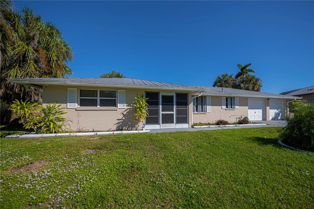 A single-story house with a tan exterior, metal roof, and attached garage under a blue sky — 2820 MARLIN PLACE, PUNTA GORDA, FL