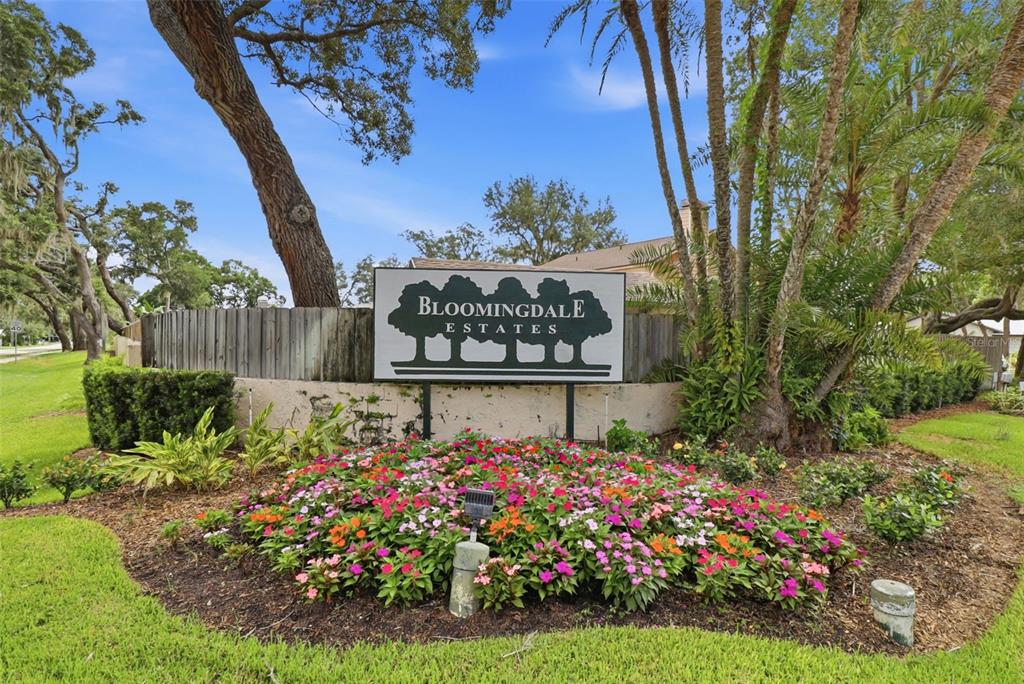 A sign for Bloomingdale Estates stands behind a colorful flower bed and mature trees — 302 BLOOMINGFIELD DRIVE, BRANDON, FL