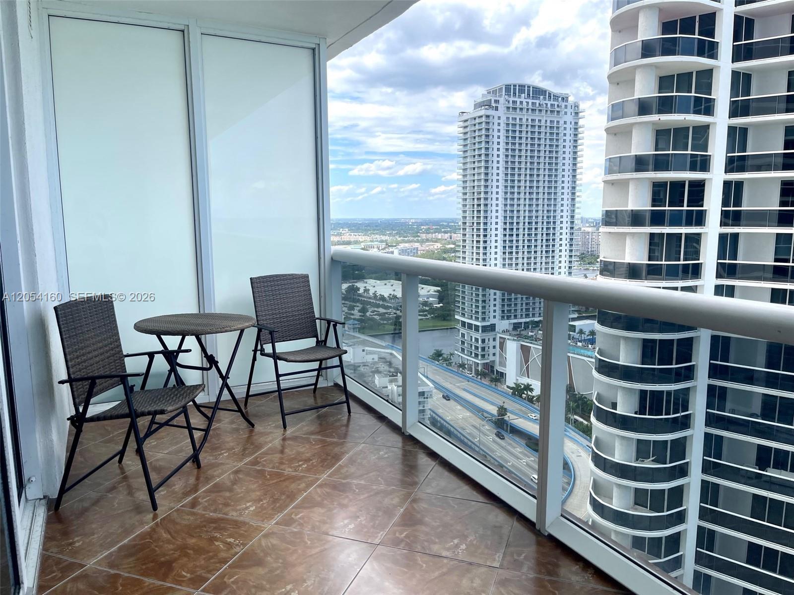 A balcony with brown tiled flooring features a small table and two chairs overlooking a city — 1830 S Ocean Dr # 3309, Hallandale Beach FL 33009, HALLANDALE BEACH, FL