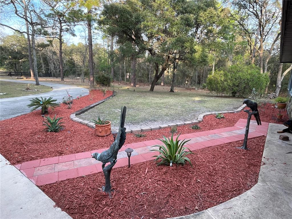 A red-mulched garden bed features a brick walkway, agave plants, and two bird statues — 4540 W SANDY HILL STREET, LECANTO, FL