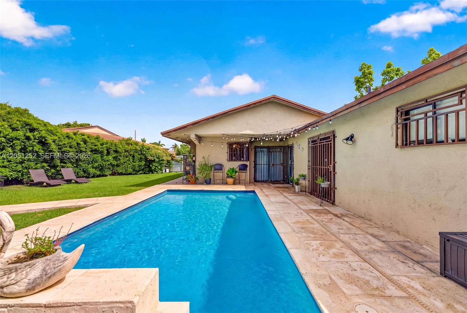 A rectangular swimming pool sits on a stone patio beside a house with exterior lighting — 12422 SW 199th St, Miami FL 33177, MIAMI, FL