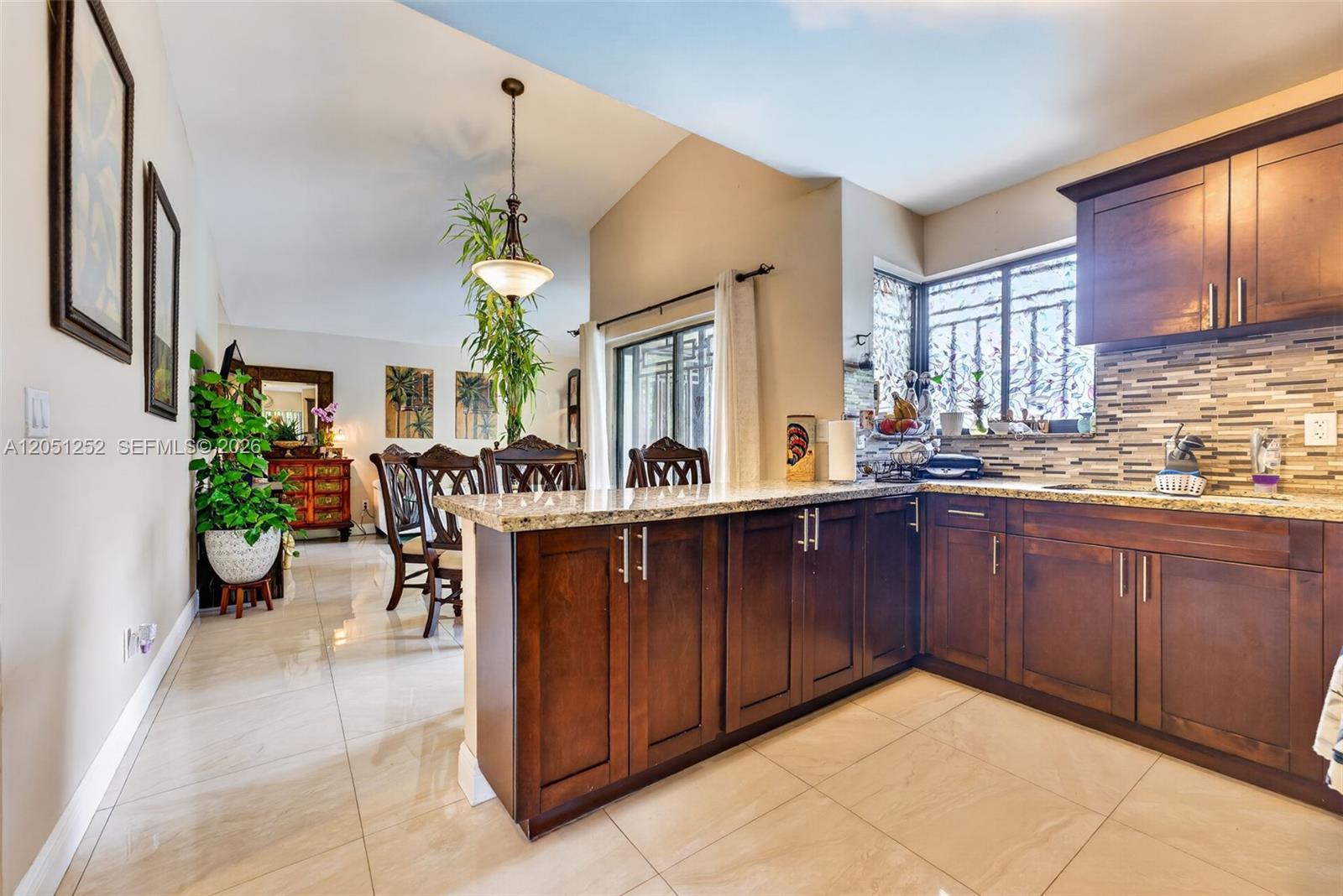A kitchen with dark wood cabinets, granite countertops, and tile flooring overlooks a dining area — 12422 SW 199th St, Miami FL 33177, MIAMI, FL