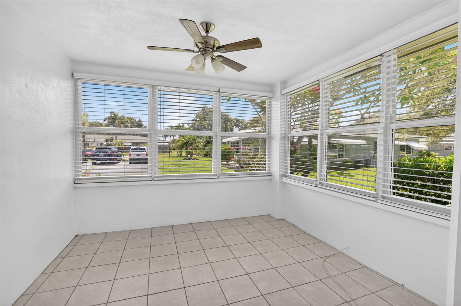 A sunroom with white walls, tiled flooring, a ceiling fan, and large windows with blinds — 912 South Drive # A, Delray Beach FL 33445, DELRAY BEACH, FL