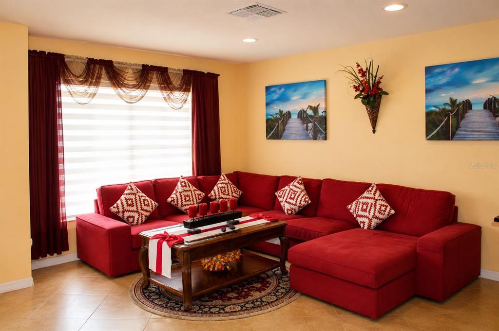 A living room features a large red sectional sofa, a coffee table, and wall art — 3513 WESTMINISTER COURT, HOLIDAY, FL