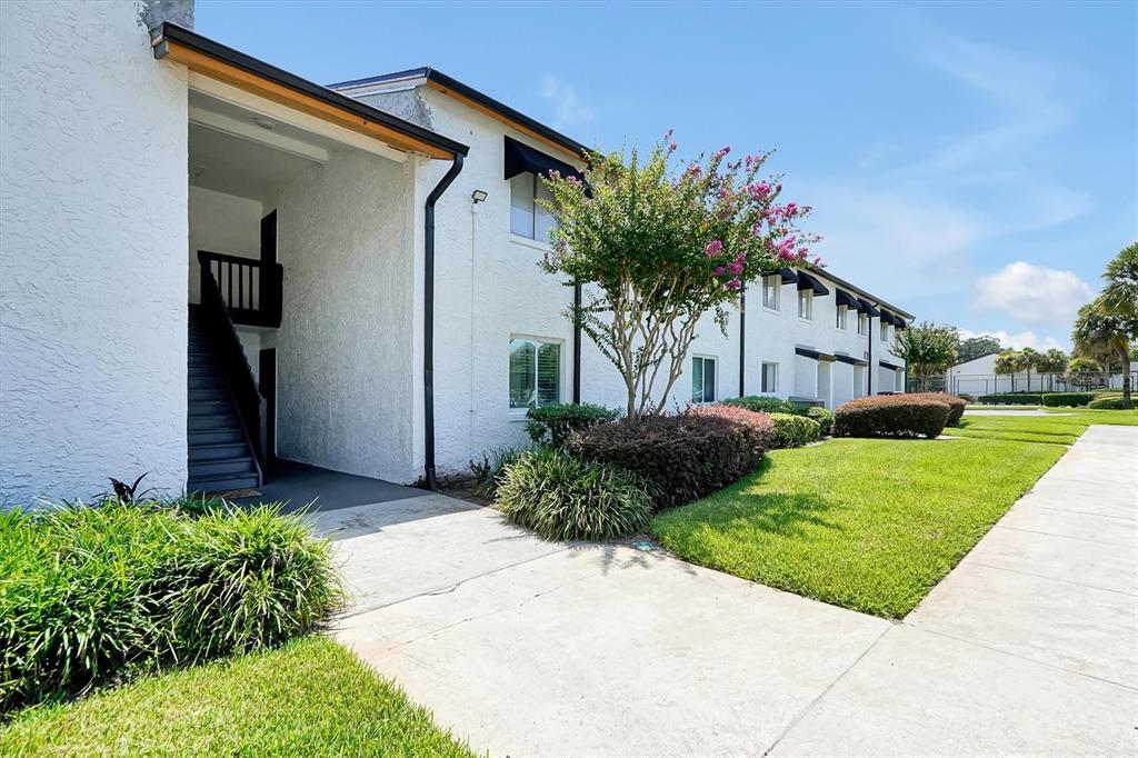A white two-story apartment building features a covered stairwell, black awnings, and landscaped grounds — 4309 N SEMORAN BOULEVARD UNIT 2, ORLANDO, FL