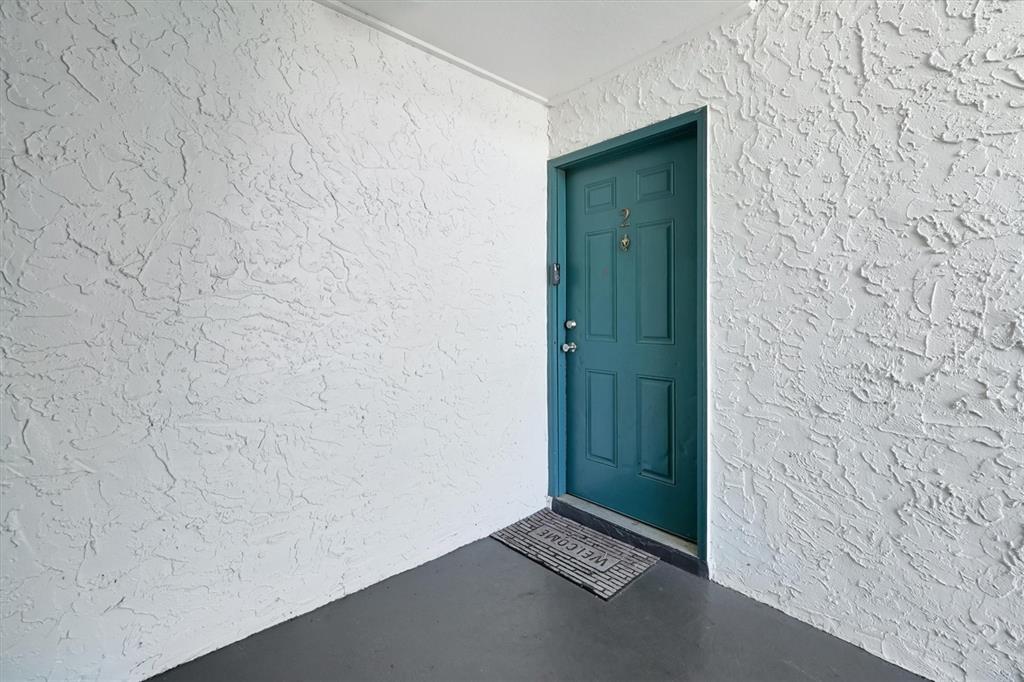 A teal front door with the number two sits against white textured walls and gray flooring — 4309 N SEMORAN BOULEVARD UNIT 2, ORLANDO, FL