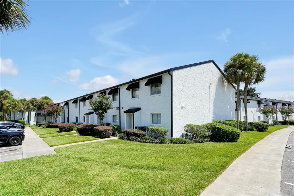 A multi-story white apartment building with black awnings sits beside a lawn and sidewalk — 4309 N SEMORAN BOULEVARD UNIT 2, ORLANDO, FL