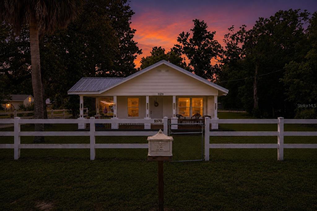 A white cottage with a front porch and a white fence at sunset — 5570 NAVARRE AVENUE, HAMPTON, FL
