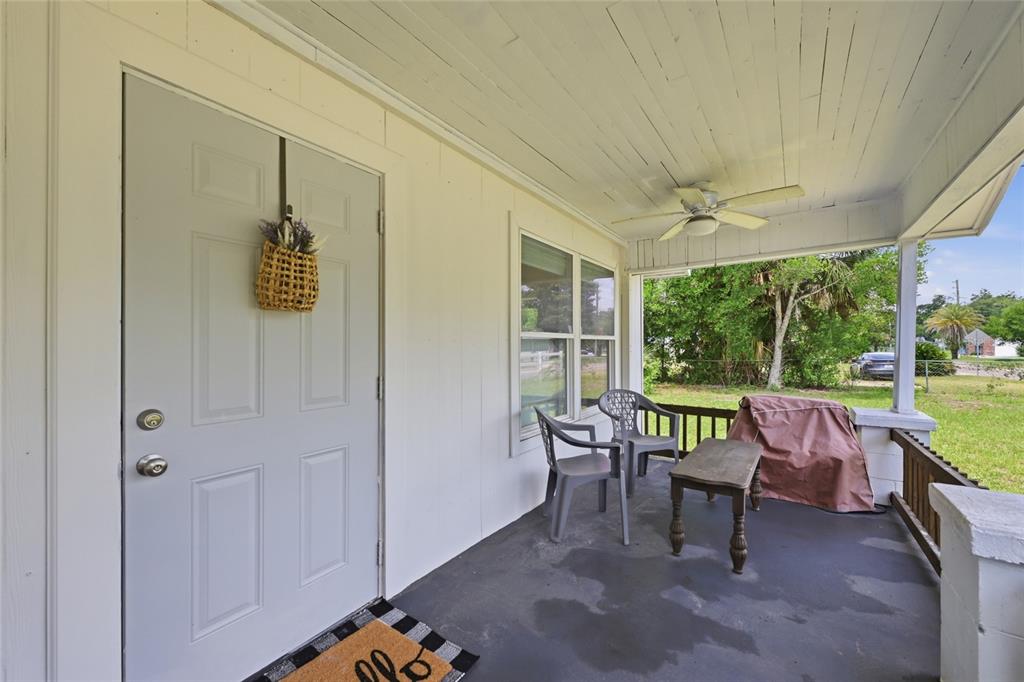 A covered front porch features a light gray door, two chairs, a table, and ceiling fan — 5570 NAVARRE AVENUE, HAMPTON, FL